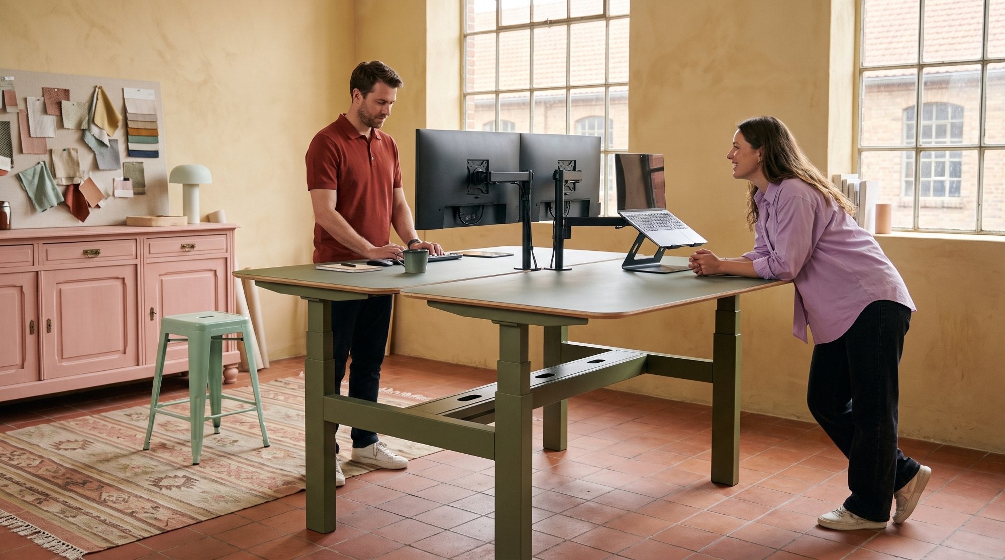 Twee collega's aan een Stadesk Duo in olijf in een atelier met okergele wanden
